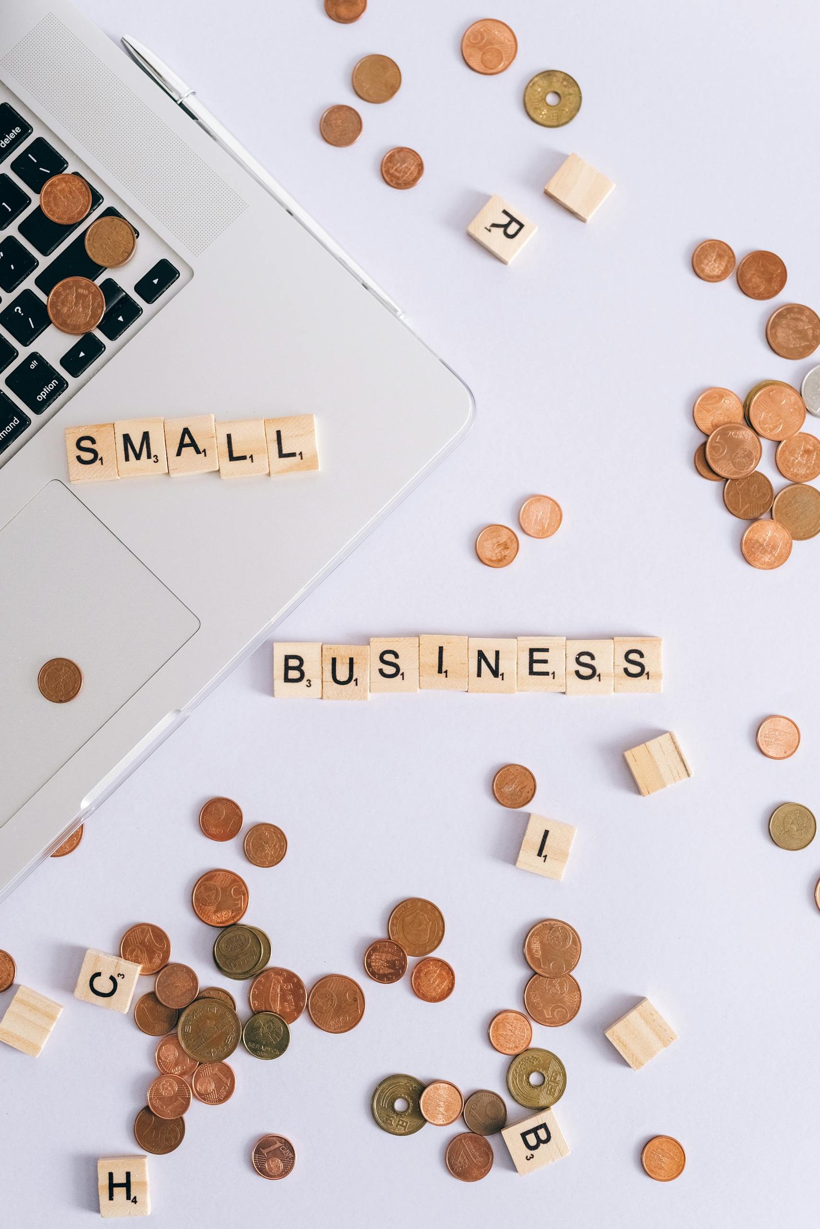 Flat lay of coins, Scrabble tiles spelling 'small business', and laptop, perfect for finance or entrepreneurship themes.